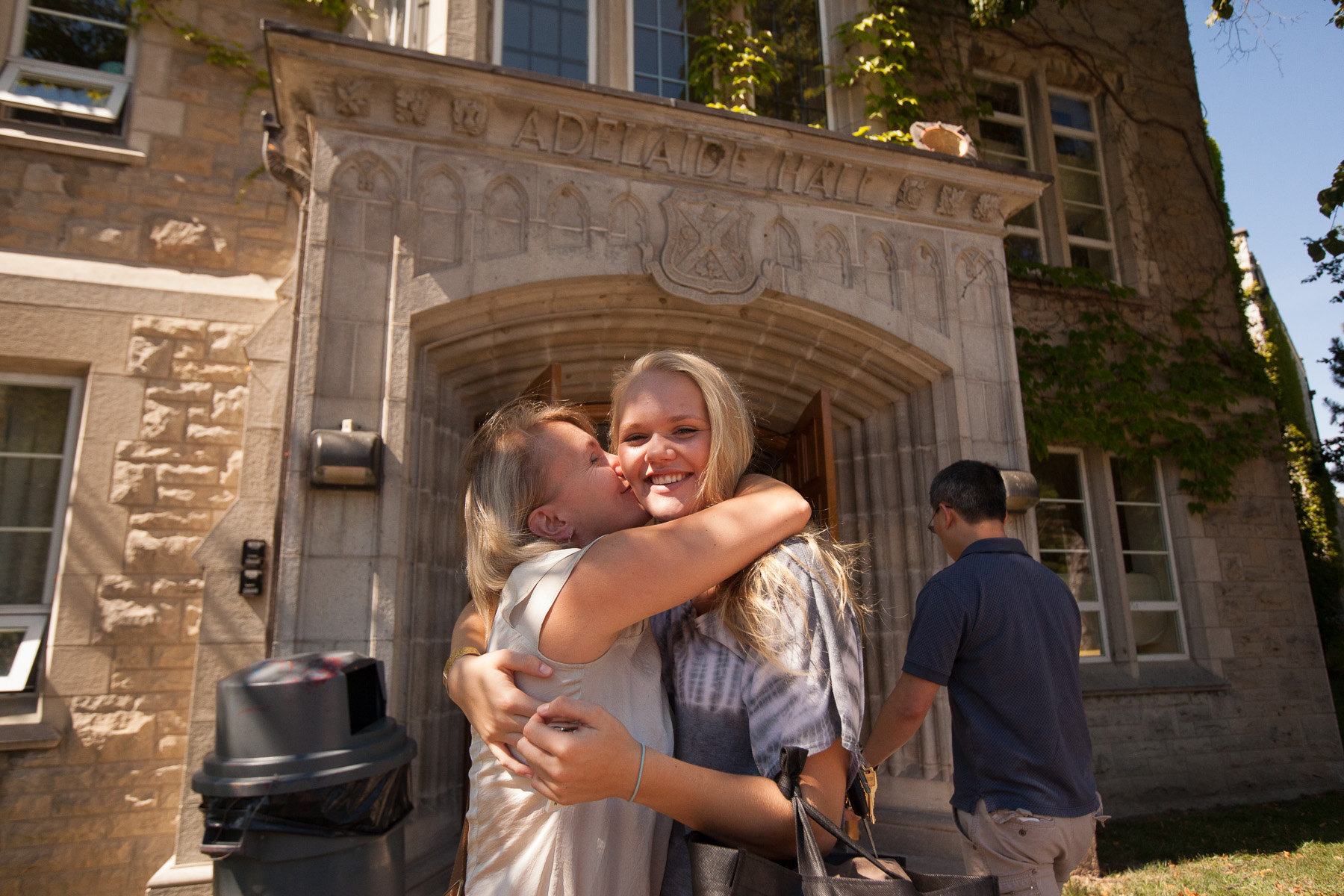 2 students outside a Queen's building hugging and kissing a cheek